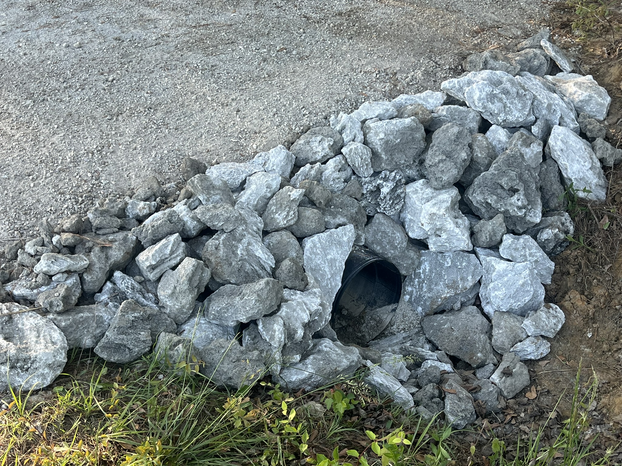 Black drainage culvert pipe surrounded by large grey rocks.